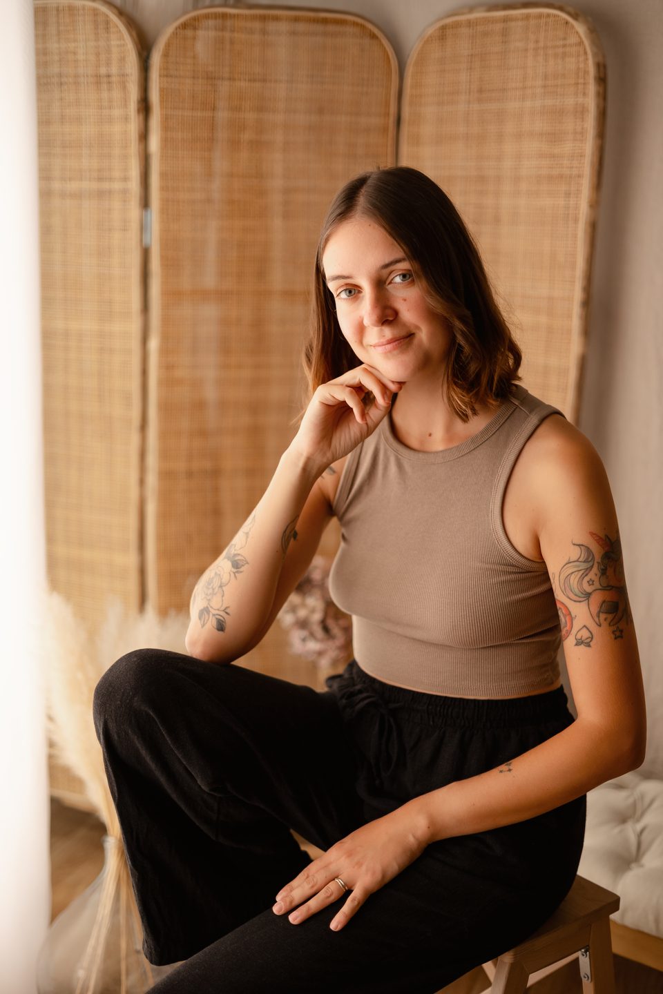 Léa Genoud, photographe, assise dans son studio devant un paravent en rotin, le menton posé sur la main.